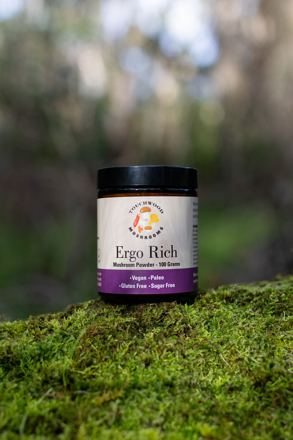 Jar of Ergo Rich mushroom powder on a mossy surface with a blurred natural background