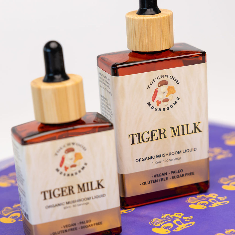 Two bottles of Tiger Milk organic mushroom liquid on a purple background with yellow tiger paw stamped print.